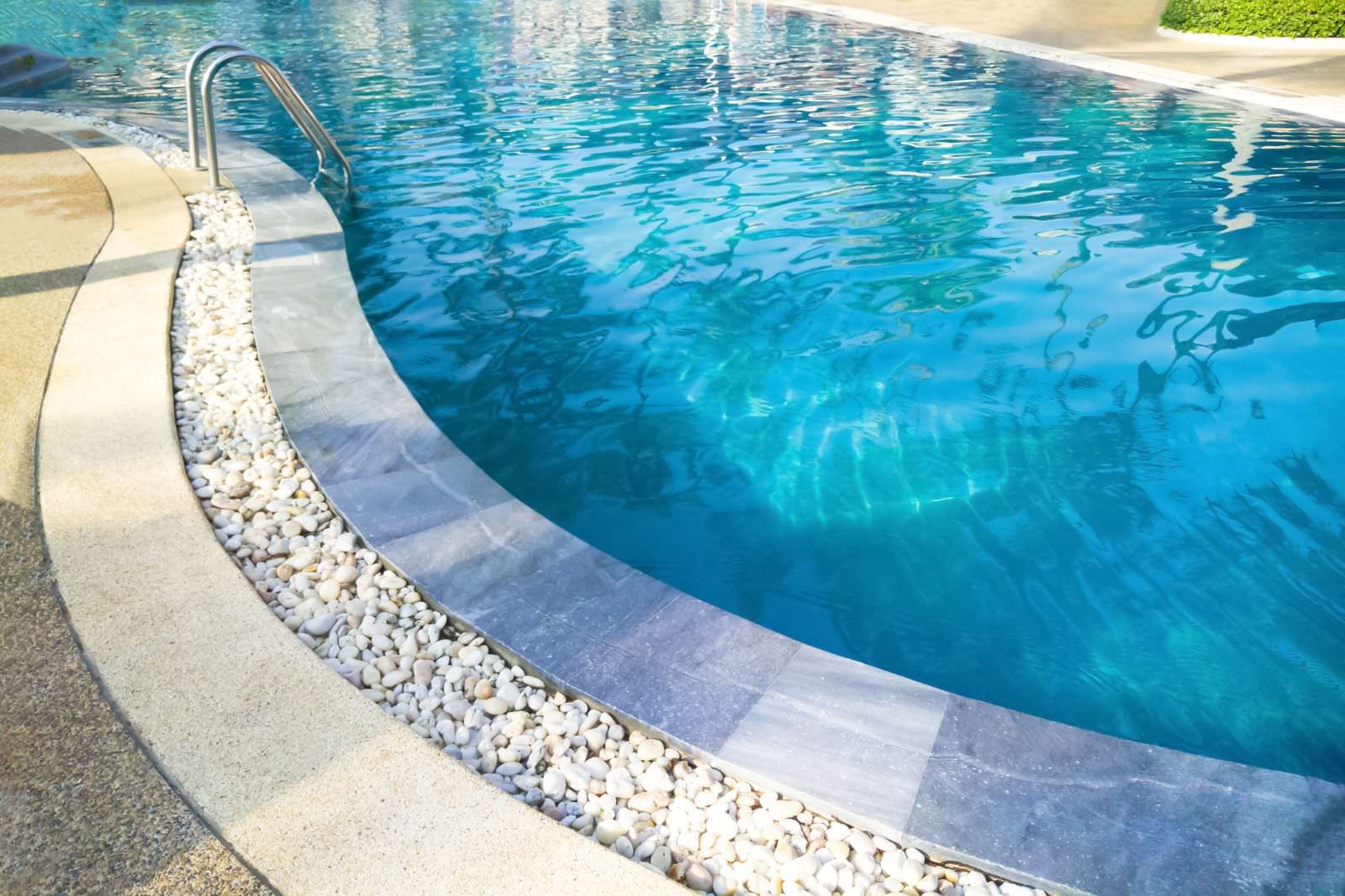 Curved residential swimming pool with clear blue water and decorative stone border in Brentwood CA