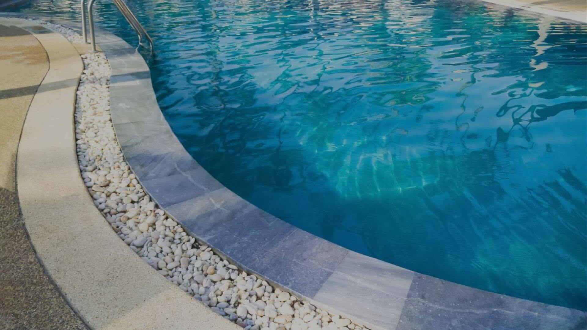 Curved residential swimming pool with clear blue water and decorative stone border in Brentwood CA