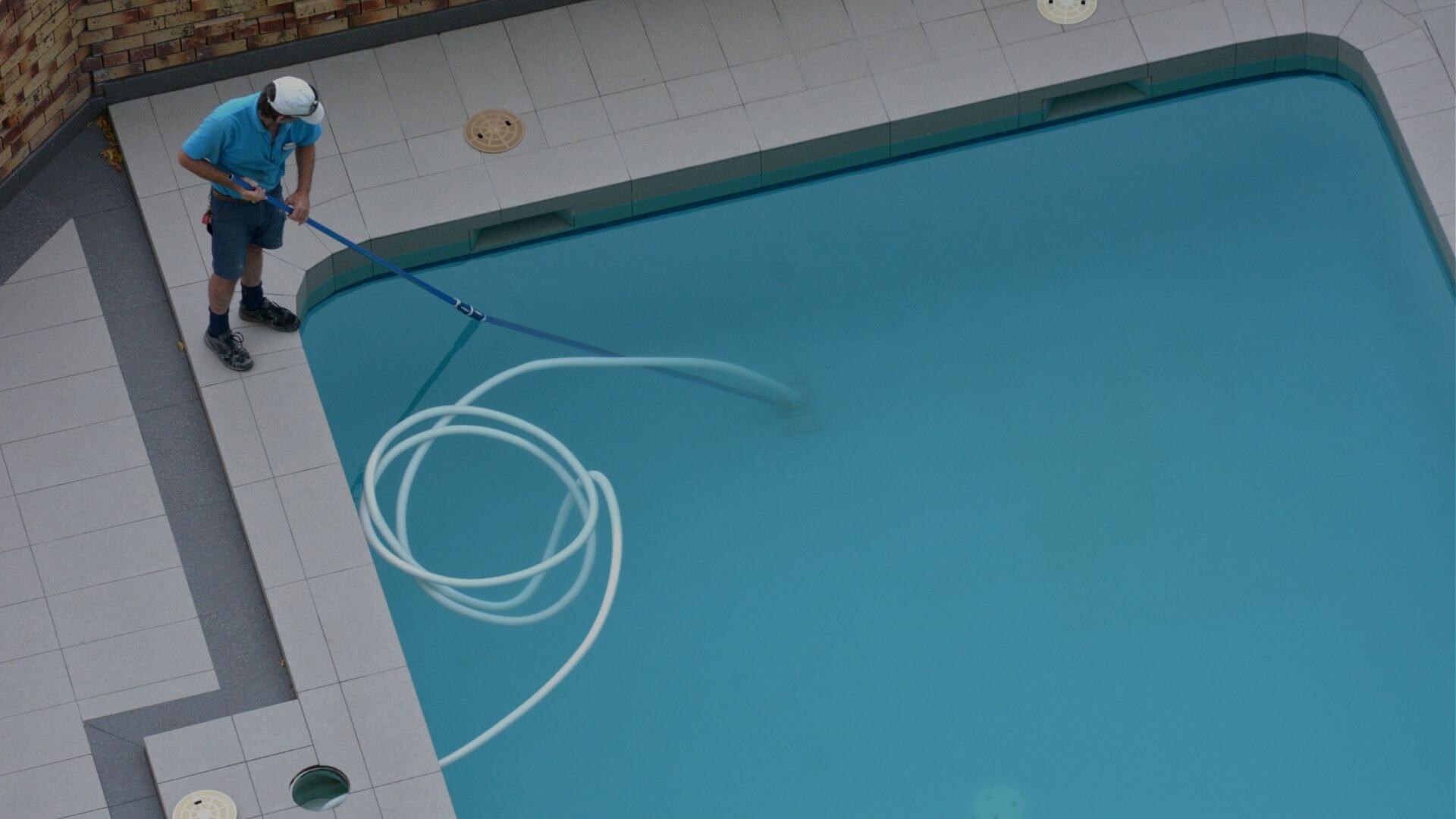 Pool service technician vacuuming residential swimming pool during routine maintenance in Brentwood CA