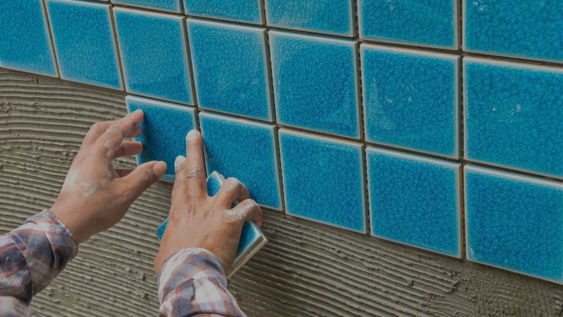 Hands installing blue ceramic tile on residential swimming pool wall during renovation in Brentwood CA